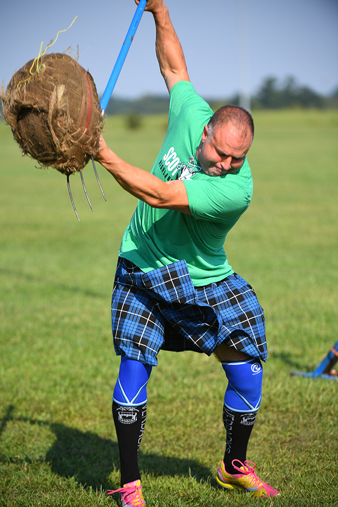 Tedd tosses a sheaf – a 16-pound burlap-covered bale of straw – with a pitchfork as high as possible.